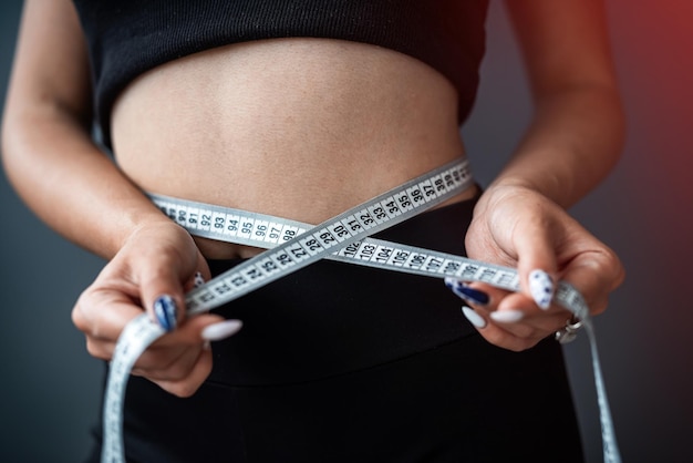 Jovem sorridente linda mulher medindo sua cintura ideal com fita métrica isolada em fundo cinza ao fundo é uma mulher no estúdio dietas estilo de vida saudável