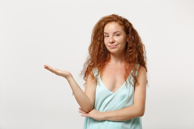 Jovem sorridente linda ruiva garota em roupas leves casuais posando isolado no retrato de estúdio de fundo branco. Conceito de estilo de vida de emoções sinceras de pessoas. Simule o espaço da cópia. Apontando a mão para o lado.