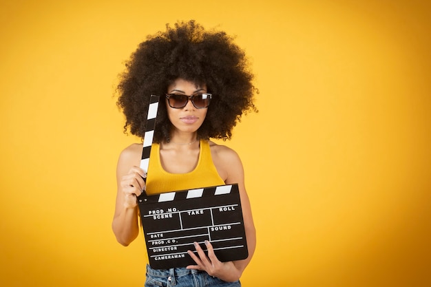 Jovem sorridente mulher afro-americana em uma calça casual posando isolado em um fundo de parede amarelo-laranja.