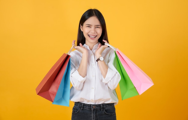 Jovem sorridente mulher asiática com roupas casuais segurando sacolas coloridas