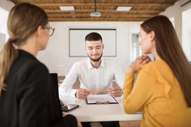 Jovem sorridente na camisa branca segurando o lápis nas mãos enquanto aguarda os resultados da entrevista de emprego