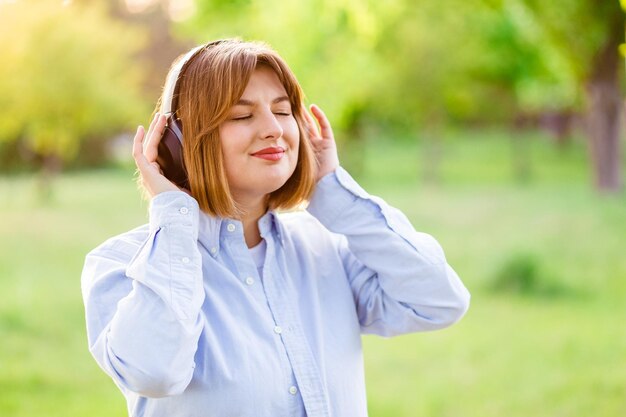 Jovem sorridente ouvindo música com fones de ouvido pretos sem fio ao pôr do sol