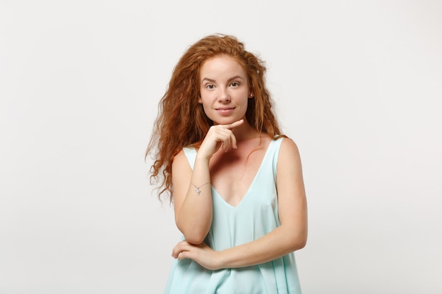 Jovem sorridente ruiva deslumbrante garota em roupas leves casuais posando isolado no fundo da parede branca, retrato de estúdio. Conceito de estilo de vida de pessoas. Simule o espaço da cópia. Coloque o apoio da mão no queixo.