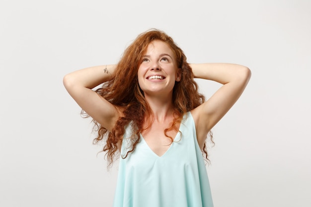 Jovem sorridente ruiva pensativa em roupas leves casuais posando isolado no fundo branco. Conceito de estilo de vida de emoções sinceras de pessoas. Simule o espaço da cópia. Olhando para cima com as mãos atrás da cabeça.