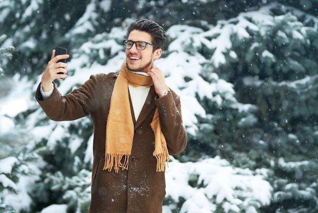 Jovem sorridente se divertindo ao ar livre. O empresário usa um telefone. Conceito de inverno. Queda de neve.