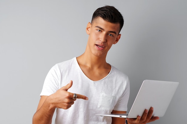 Jovem sorridente segurando laptop sobre fundo cinza