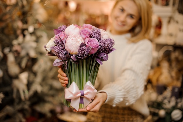 Jovem sorridente segurando um buquê de flores macias de cor rosa e roxo com hastes verdes