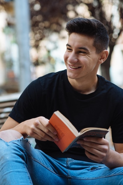 Jovem sorridente segurando um livro enquanto estava sentado ao ar livre