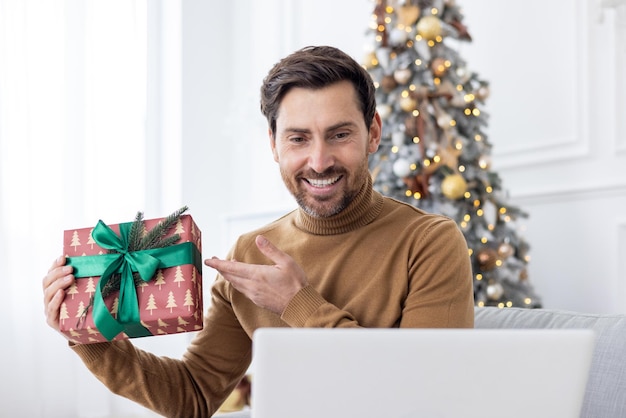 Jovem sorridente sentado em casa no sofá perto da árvore de natal nos feriados de ano novo e