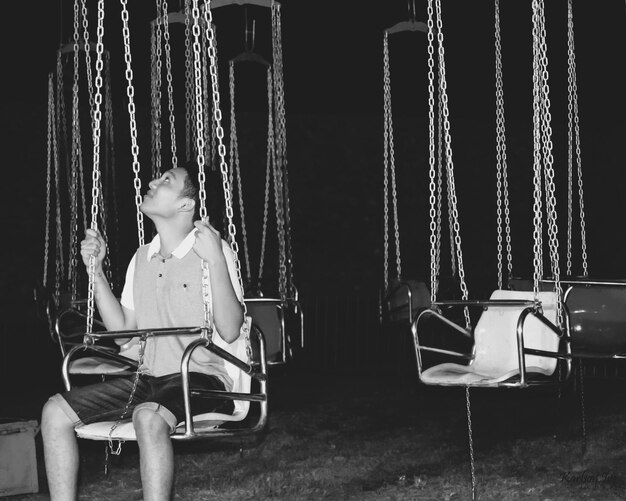 Foto jovem sorridente sentado em um balanço de cadeia à noite