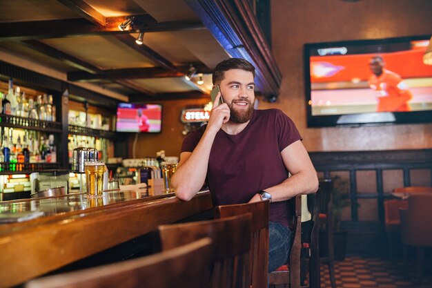 Jovem sorridente sentado em um bar falando no celular