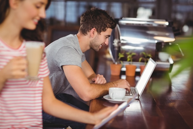 Jovem sorridente sentado no bar e usando laptop