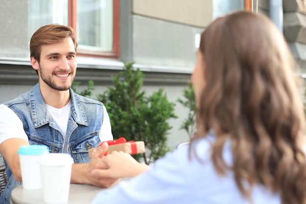 Jovem sorridente tendo um encontro com o namorado no café, homem segurando uma caixa de presente.