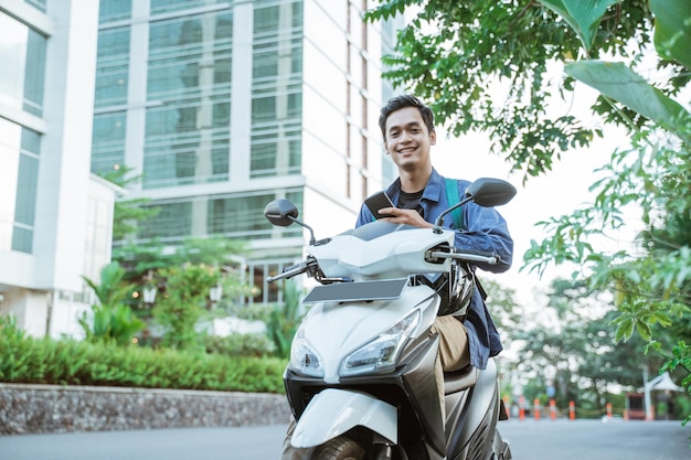 Jovem sorridente usando um celular ao andar de moto no fundo da rua da cidade