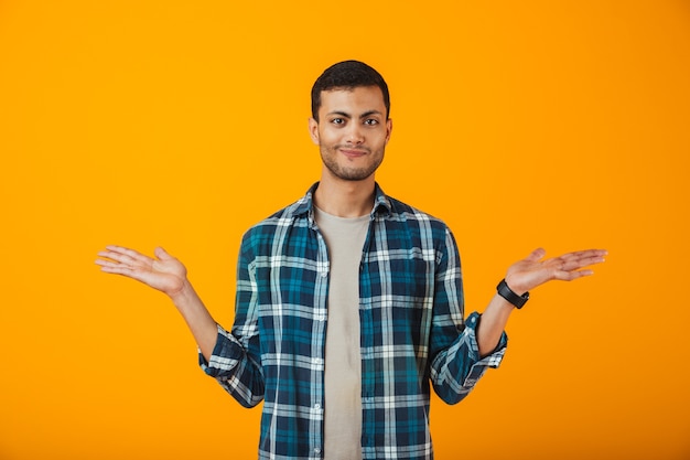 Jovem sorridente, vestindo uma camisa xadrez, isolado na parede laranja, mostrando o espaço da cópia