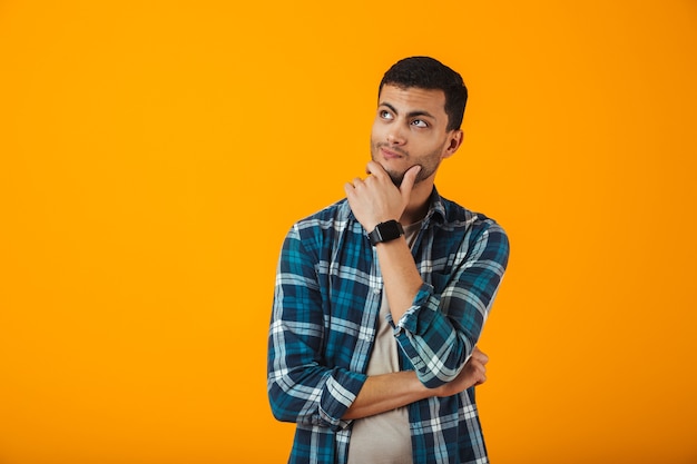 Jovem sorridente, vestindo uma camisa xadrez, isolado na parede laranja, olhando para longe