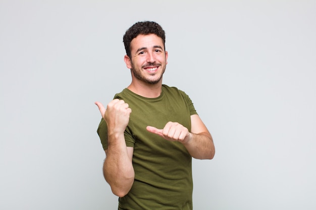 Jovem sorrindo alegre e casualmente apontando para uma cópia do espaço ao lado, sentindo-se feliz e satisfeito