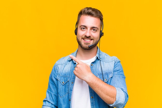 Jovem sorrindo alegremente, sentindo-se feliz e apontando para o lado e para cima, mostrando o objeto no espaço da cópia