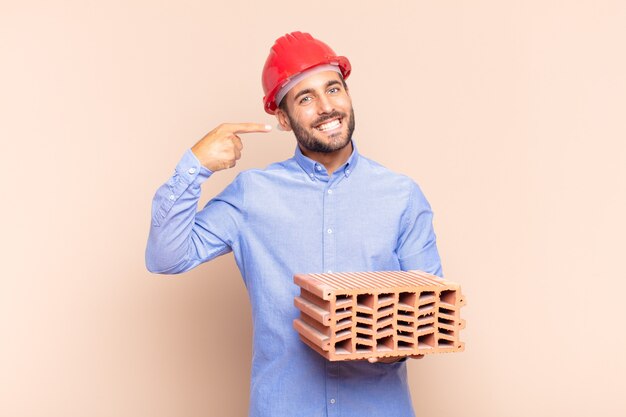 Jovem sorrindo com confiança, apontando para o próprio sorriso largo, atitude positiva, relaxada e satisfeita. conceito de arquiteto