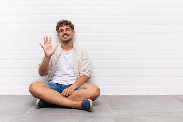 Jovem sorrindo e parecendo amigável, mostrando o número cinco ou quinto com a mão para a frente, em contagem regressiva