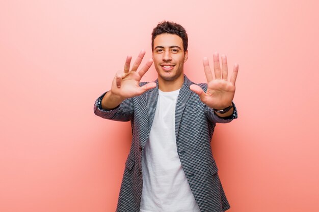 Jovem, sorrindo e parecendo amigável, mostrando o número nove ou nono com a mão para a frente, contando a parede rosa