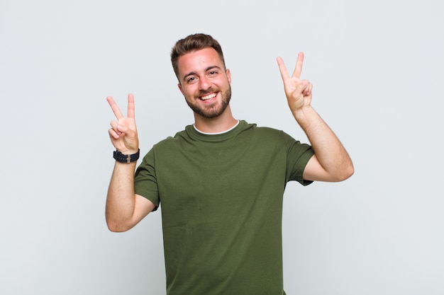 Jovem sorrindo e parecendo feliz, amigável e satisfeito, gesticulando vitória ou paz com as duas mãos