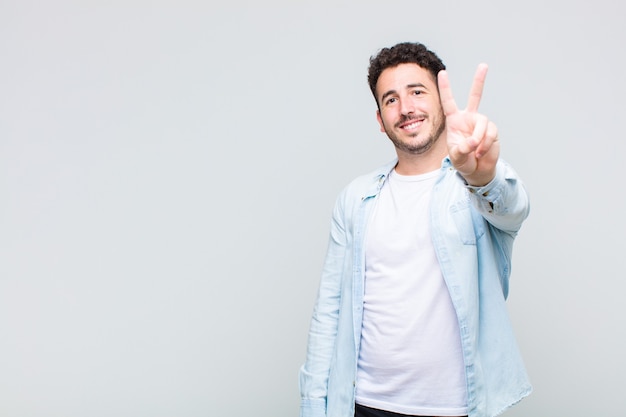 Jovem sorrindo e parecendo feliz, despreocupado e positivo, gesticulando vitória ou paz com uma mão