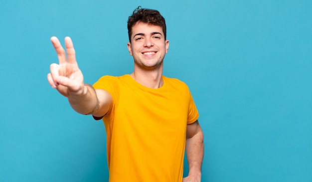 Jovem sorrindo e parecendo feliz, despreocupado e positivo, gesticulando vitória ou paz com uma mão