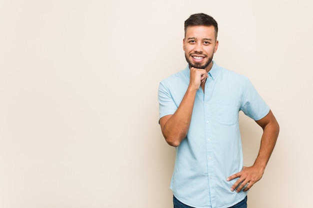 Jovem sorrindo feliz e confiante, tocando o queixo com a mão.