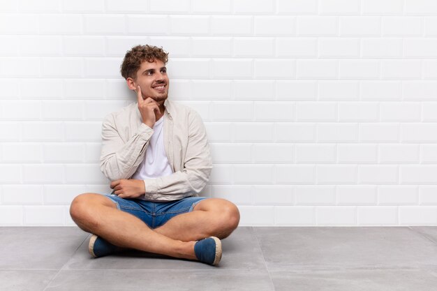 Jovem sorrindo feliz e sonhando acordado ou duvidando, olhando para o lado