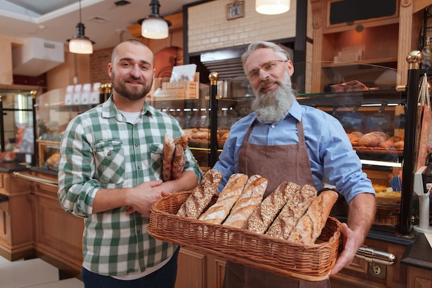 Jovem sorrindo para a câmera enquanto compra pão do padeiro sênior