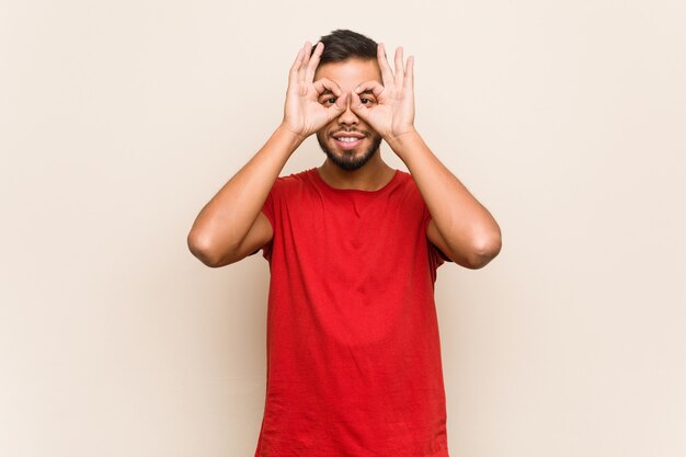 Jovem sul-asiático mostrando sinal bem sobre os olhos