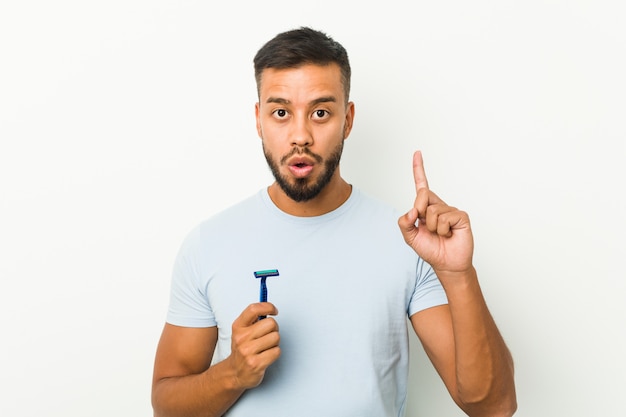 Jovem sul-asiático segurando uma lâmina de barbear, tendo uma ótima idéia, conceito de criatividade.