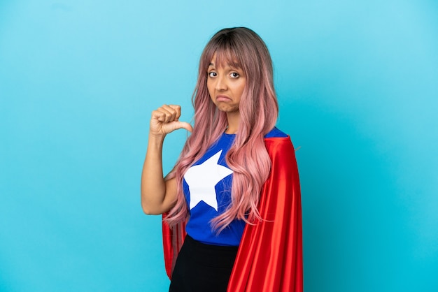 Jovem super-heroína com cabelo rosa isolada em um fundo azul, orgulhosa e satisfeita