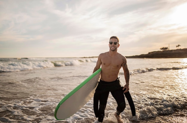 Jovem surfista atlético de fato de mergulho caminhando com uma prancha de surf na praia