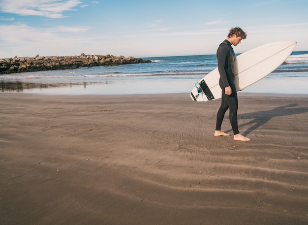 Jovem surfista em pé no oceano com sua prancha de surf em um terno preto de surf. esporte e conceito de esporte aquático.