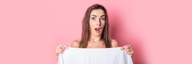 Foto jovem surpreendida com o cabelo molhado nu se escondendo atrás da toalha no fundo rosa