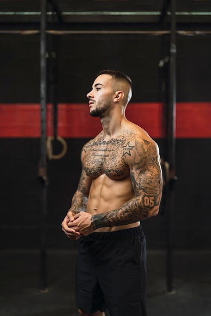 Foto jovem tatuado fazendo esportes em uma academia com pesos e máquina de remo