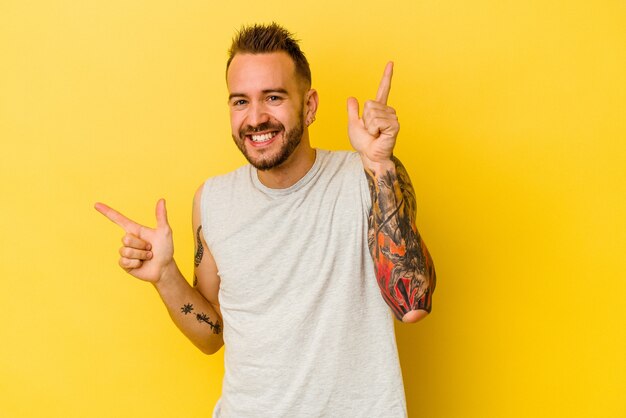 Jovem tatuado homem caucasiano isolado em fundo amarelo, apontando para diferentes espaços de cópia, escolhendo um deles, mostrando com o dedo.