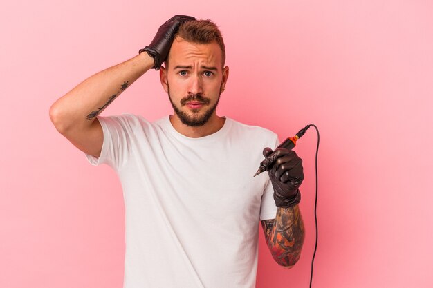 Jovem tatuador caucasiano isolado em um fundo rosa sendo chocado, ela se lembrou de um encontro importante.