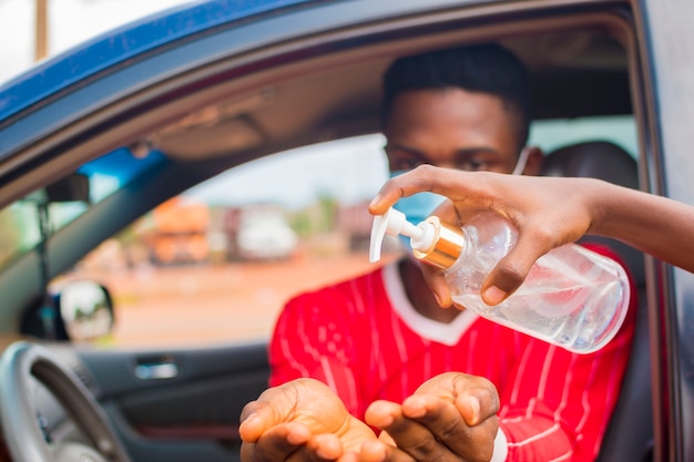 Jovem taxista africano usando máscara facial previne, previne, se previne de surto na sociedade e usa desinfetante para as mãos para lavar as mãos