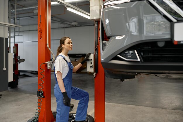 Jovem técnica de automóveis ligando o mecanismo de elevação do carro enquanto trabalha em uma oficina de reparo