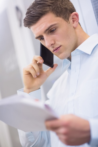 Jovem técnico ligando e lendo um documento