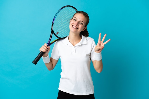 Jovem tenista isolada na parede azul feliz e contando três com os dedos