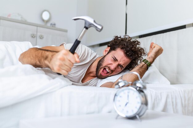 Jovem tenta quebrar o despertador com o martelo, Destroy the Clock. Homem deitado na cama, desligando o despertador com um martelo às 7h da manhã.