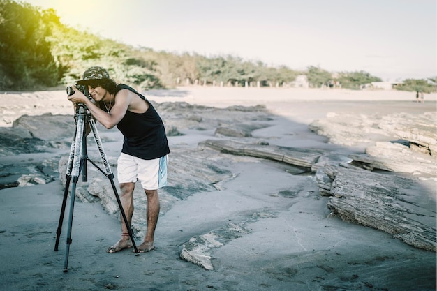 Jovem tirando foto na praia homem fotografando com tripé no mar