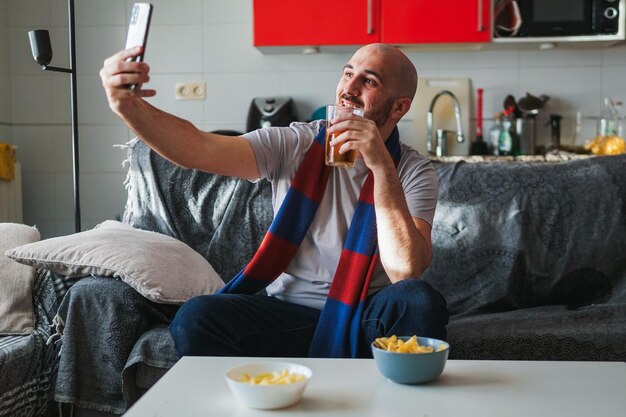 Foto jovem tirando uma selfie enquanto assiste esportes no sofá