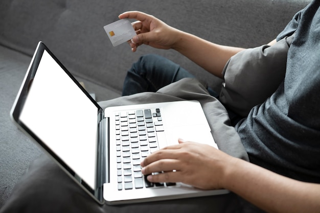 Jovem tiro recortado sentado no sofá e compras online ou assando online com o laptop do computador.