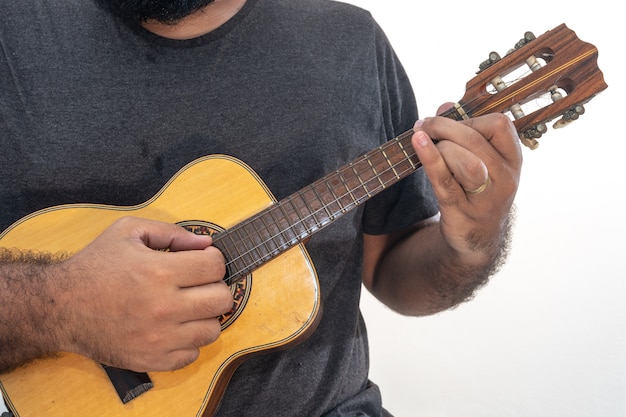 Jovem tocando cavaquinho com camisa e calça preta.