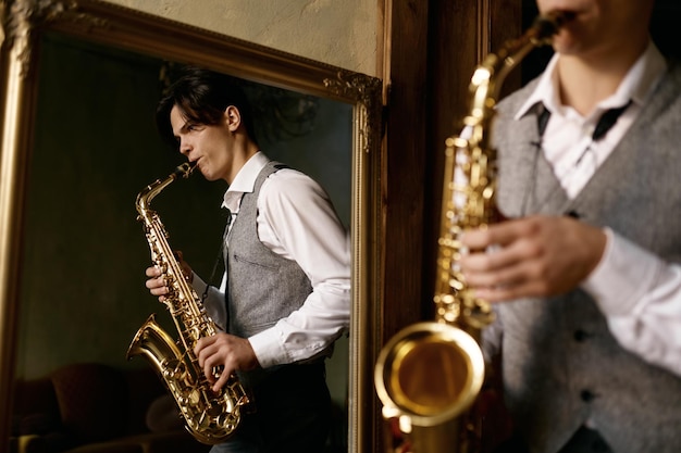 Jovem tocando saxofone no reflexo do espelho em casa. Apaixonado por música